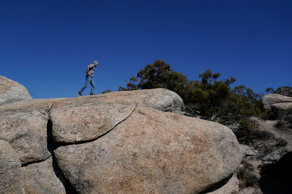An asylum-seeker tries to find cell phone signal by climbing up rocks after crossing the...