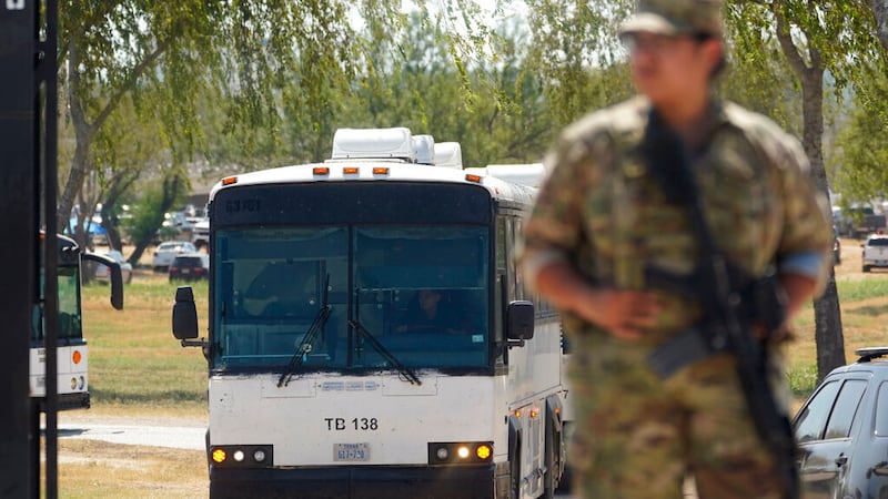 A National Guardsman stands at a gate along a border fence as a bus used to transport...